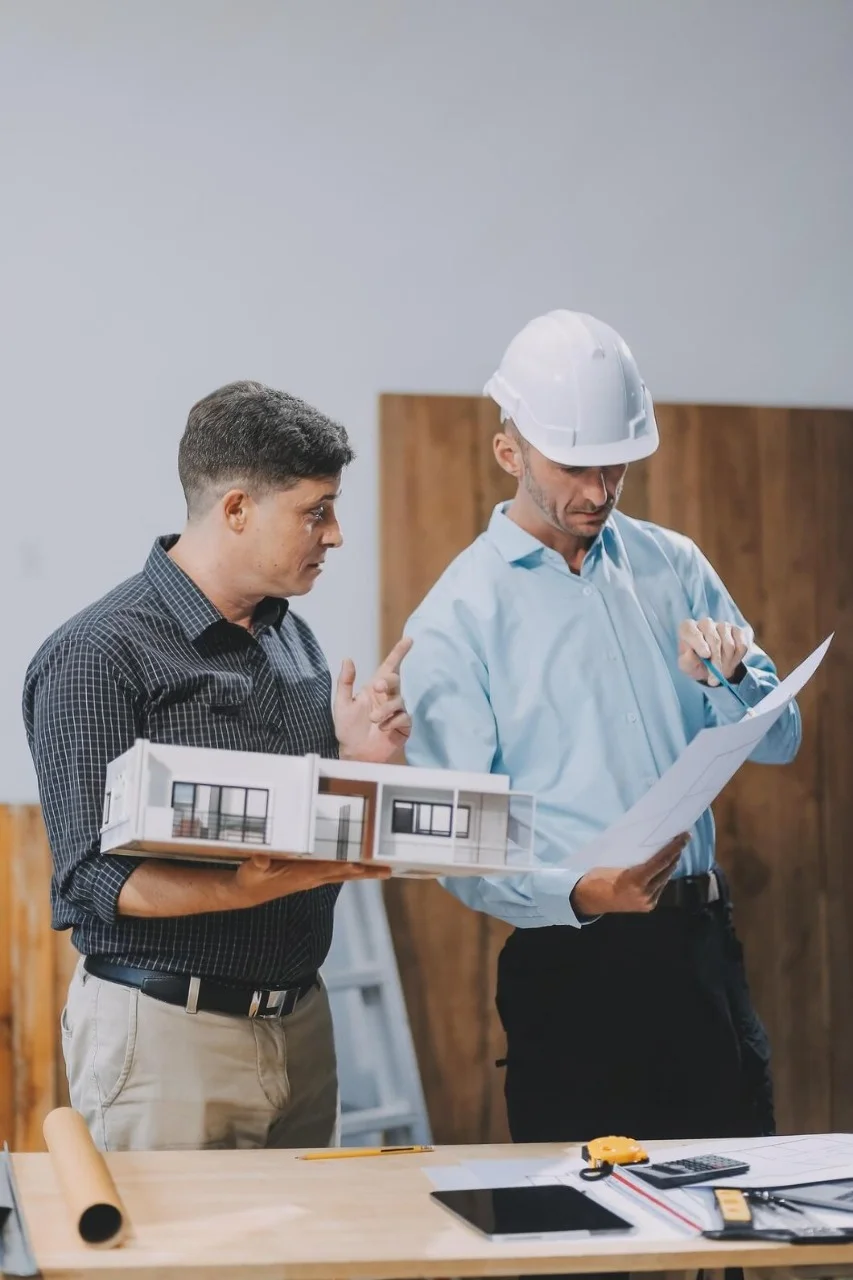 Engineers reviewing blueprints and a house model, symbolizing CESOL’s construction expertise.
